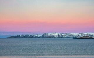 incroyable lever du soleil polaire paysage avec blanc neigeux Montagne intervalle sur le horizon. Arctique océan panoramique vue photo