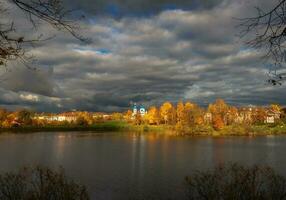 blanc cathédrale dans le distance entouré par d'or l'automne des arbres. le village avant le tempête. gatchina vieux ville. photo