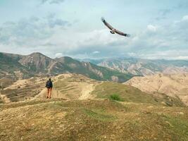 une Masculin touristique avec une sac à dos montres le vol de un Aigle contre le toile de fond de magnifique haute montagnes. photo