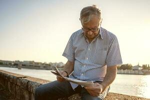 Sénior homme en train de lire une livre à l'extérieur photo