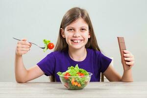 une fille choisir entre salade et une Chocolat bar photo