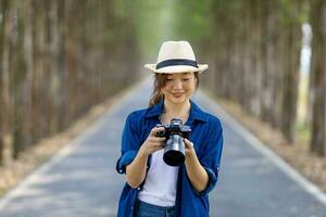 asiatique touristique femme est prise photo en utilisant professionnel caméra tandis que ayant vacances à le nationale parc tandis que en marchant sur le route avec colonne de arbre pour Voyage et la photographie concept