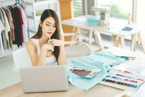 Jeune adulte asiatique femme tailleur designer en utilisant portable ordinateur pour l'Internet en ligne commercialisation contact client photo