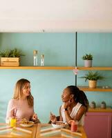 Jeune noir et caucasien femme ayant bien temps, en buvant Frais jus et ayant en bonne santé petit déjeuner dans le café photo