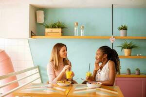 Jeune noir et caucasien femme ayant bien temps, en buvant Frais jus et ayant en bonne santé petit déjeuner dans le café photo