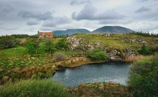 magnifique paysage paysage avec vieux rouillé étain toit chalet par le rivière avec montagnes dans le Contexte à connemara nationale parc dans comté Galway, Irlande photo