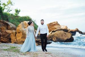 Mariée dans une robe bleue avec le marié marchant le long du rivage de l'océan photo