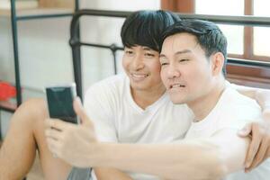 content asiatique gay couple utilisation mobile téléphone vidéo appel ou selfie sur lit, lgbtq concept. content gay couple ayant amusement en utilisant mobile téléphone intelligent dans lit. la diversité de lgbt des relations. photo
