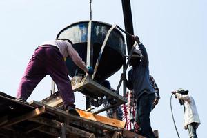 groupe de travailleurs chargeant le ciment mélangé à partir du godet en acier sur le chantier de construction. photo