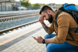 adulte homme est séance à chemin de fer station et attendre pour arrivée de train. photo