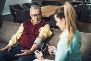 Accueil médecin est mesure du sang pression de vieux homme à le sien maison. professionnel santé soutien pour personnes âgées personnes. photo