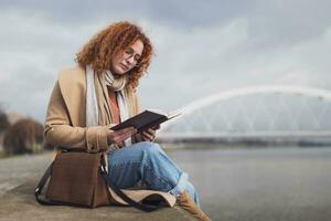 Naturel portrait de une caucasien gingembre femme avec taches de rousseur et frisé cheveux. elle est en train de lire livre. photo