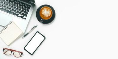 Haut voir, blanc Bureau bureau avec portable ordinateur, Vide écran intelligent téléphone, tasse de café, stylo et carnet de notes, copie espace, moquer en haut.. photo