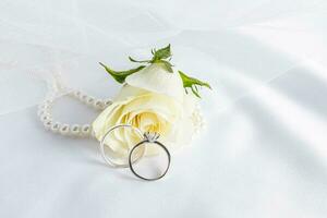 deux engagement anneaux avec une diamant sur une Contexte de Frais thé Rose et perle perles. doux satin tissu. espace pour texte. disposition conception. photo