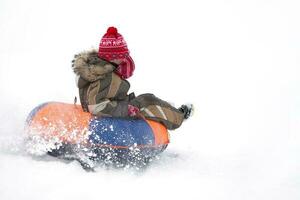 enfant dans l'hiver. de bonne humeur garçon est équitation un gonflable traîneau. photo