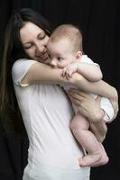 magnifique mère câlins sa bébé. maternité.maman et peu fils sur une foncé Contexte. maternité. photo