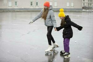 les enfants la glace patinage sur le ville patinage patinoire. le plus âgée sœur enseigne le plus jeune un à patin. photo