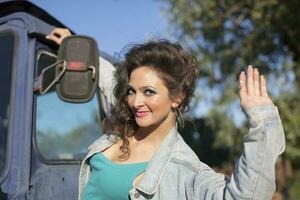 magnifique Jeune femme dans une denim veste posant contre le toile de fond de une tracteur. fille dans le style de le années quatre-vingt. photo