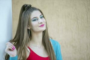 portrait de une brunette fille avec brillant maquillage près une beige mur. photo