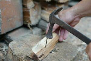 fermer Charpentier utilisation vieux marteau à frappé métal clou sur bois. concept, charpenterie et construction outils. réparation ou fixation, DIY boiseries. local mode de vie. photo