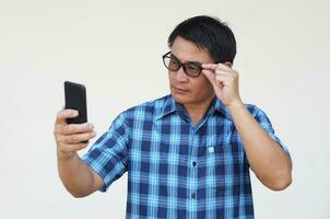 asiatique homme a problème avec vue , porte lunettes, détient téléphone intelligent. concept, vue problème. optométrie. photo