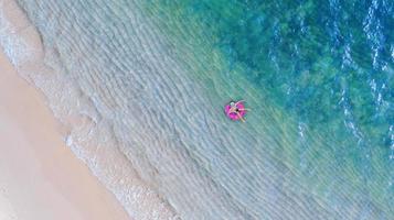 Vue aérienne de dessus du drone vue du garçon avec anneau de bain dans la mer et l'ombre bleu émeraude de l'eau et de la mousse de vague au lever du soleil