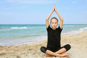 fille pratiquant yoga sur plage. adolescent est séance dans lotus position. photo