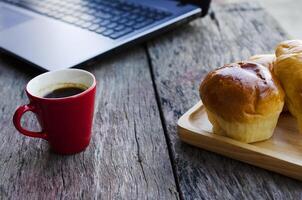 Tasse à café rouge et petits pains savoureux avec ordinateur portable sur table en bois pour nomade numérique de la technologie de style de vie photo