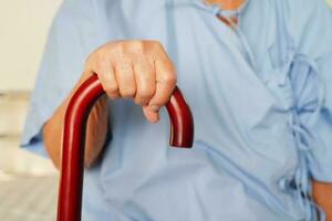 asiatique personnes âgées invalidité femme patient en portant en marchant bâton dans ridé main à hôpital. photo