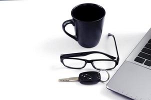 café noir, ordinateur portable, lunettes et clés de voiture sur fond blanc photo
