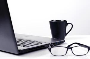 Gros plan de tasses à café avec ordinateur de laboratoire et lunettes sur fond blanc photo