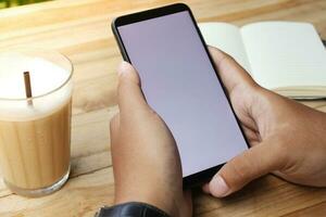 proche en haut de Masculin main en utilisant mobile téléphone dans Vide écran avec vide carnet et une tasse de café tandis que séance à café photo