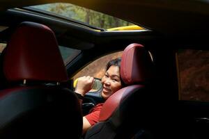 femme asiatique au volant d'une voiture jaune toit en boucle soleil ouvert sourire heureux elle a jeté un coup d'œil derrière elle, regardant à travers la porte arrière droite de la voiture. pendant la conduite d'un week-end. mise au point douce et sélective. photo