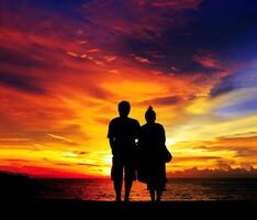 Jeune couple permanent sur le plage dans le direction de mer à la recherche vers magnifique rouge ciel. romantique silhouette art de relation ai généré photo