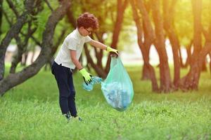 Jeune garçon ramasse les ordures dans une forêt de printemps au coucher du soleil photo