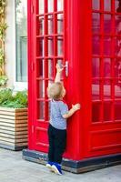 une peu garçon veut à entrer une rouge téléphone stand. photo