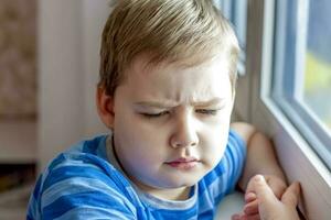 le enfant émotions. les enfants. portrait de une garçon. une triste expression sur le sien affronter. triste à le la fenêtre. photo