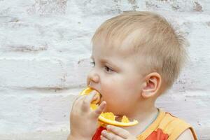 portrait de enfant. mignonne garçon posant et en mangeant une délicieux orange. le émotions de une enfant. photo