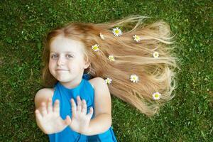 portrait d'une belle petite fille aux cheveux rouges en bonne santé avec des fleurs de camomille allongées sur l'herbe photo