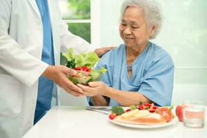 asiatique personnes âgées femme patient en mangeant Saumon steak petit déjeuner avec légume en bonne santé nourriture dans hôpital. photo