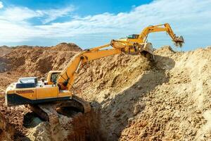 deux excavatrice sont creusement sol dans le construction site sur ciel arrière-plan, avec blanc duveteux nuage photo