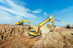 deux excavatrice sont creusement sol dans le construction site sur ciel arrière-plan, avec blanc duveteux nuage photo