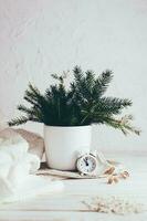 organisation de une de fête Noël tableau. sapin bouquet dans une vase, blanc alarme l'horloge et une confortable chandail sur une blanc en bois tableau. respectueux de la nature et fait maison mode de vie. verticale vue photo