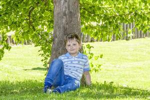 le garçon est séance dans le ombre en dessous de une arbre. cache de le Soleil photo