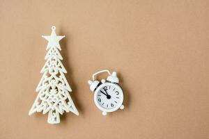 concept compte à rebours sur Noël nuit. blanc alarme l'horloge à cinq à Douze et une décoratif Noël arbre sur beige papier carton. Haut voir. copie espace photo