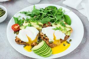 en bonne santé petit déjeuner. poché des œufs sur pain grillé avec Avocat pièces, roquette, mizuna et bettes feuilles et Cerise tomates sur une assiette sur une servi tableau. flexétaire régime. fermer photo