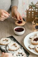 enfants mains propager baie confiture sur linzer biscuits sur le cuisine tableau. cuisine Noël traite. mode de vie. verticale vue photo