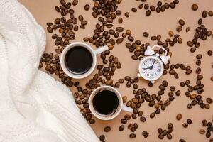 deux tasses de noir café, alarme horloge, blanc chandail et café des haricots sur une beige Contexte. confortable Date et bien-être. Haut vue photo