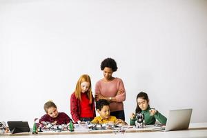 Des enfants heureux avec leur professeur de sciences afro-américaine programmant des jouets électriques et des robots en classe de robotique photo