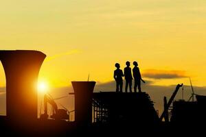 silhouette d'ingénieur et de travailleur vérifiant le projet sur le fond du chantier, chantier de construction au coucher du soleil le soir photo